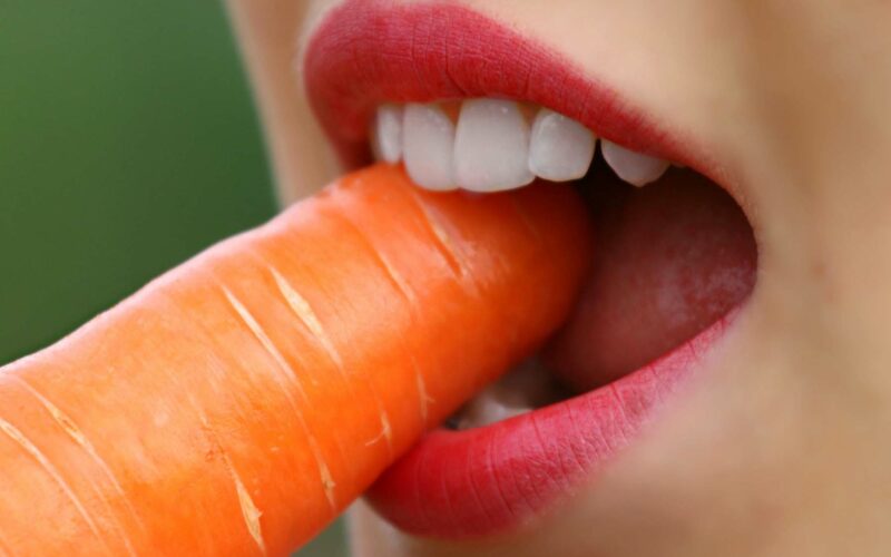 woman eating carrot to get vitamins for strong teeth