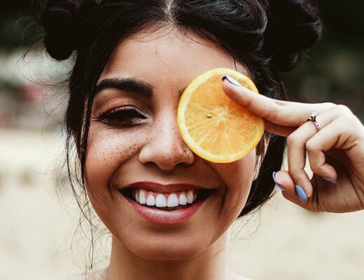 woman smiling holding orange to face showing vitamins for healthy gums