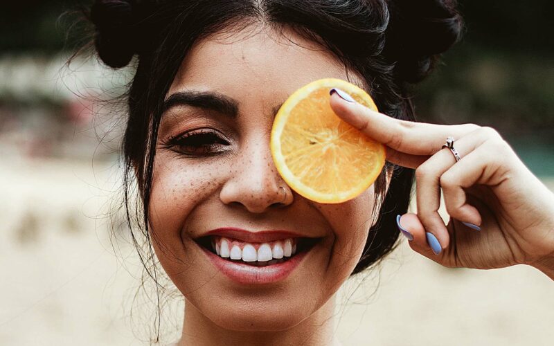 woman smiling holding orange to face showing vitamins for healthy gums