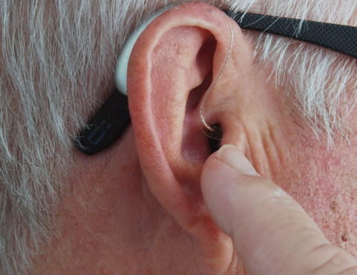 grey haired man using hearing aid due to hearing loss