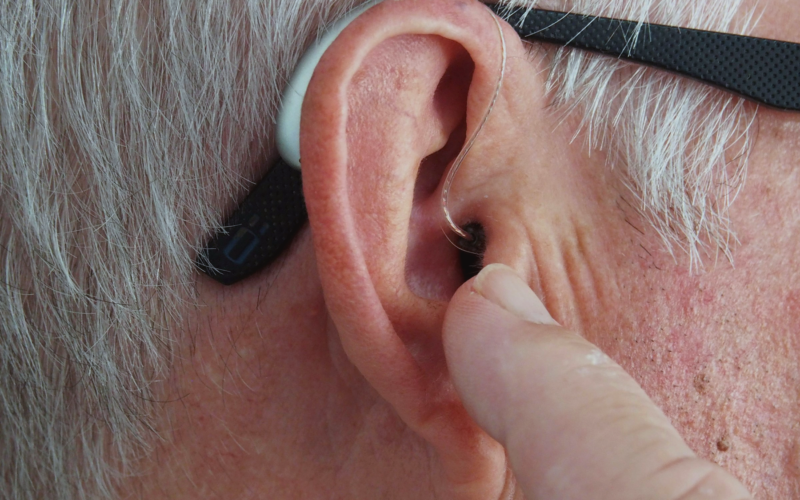 grey haired man using hearing aid due to hearing loss